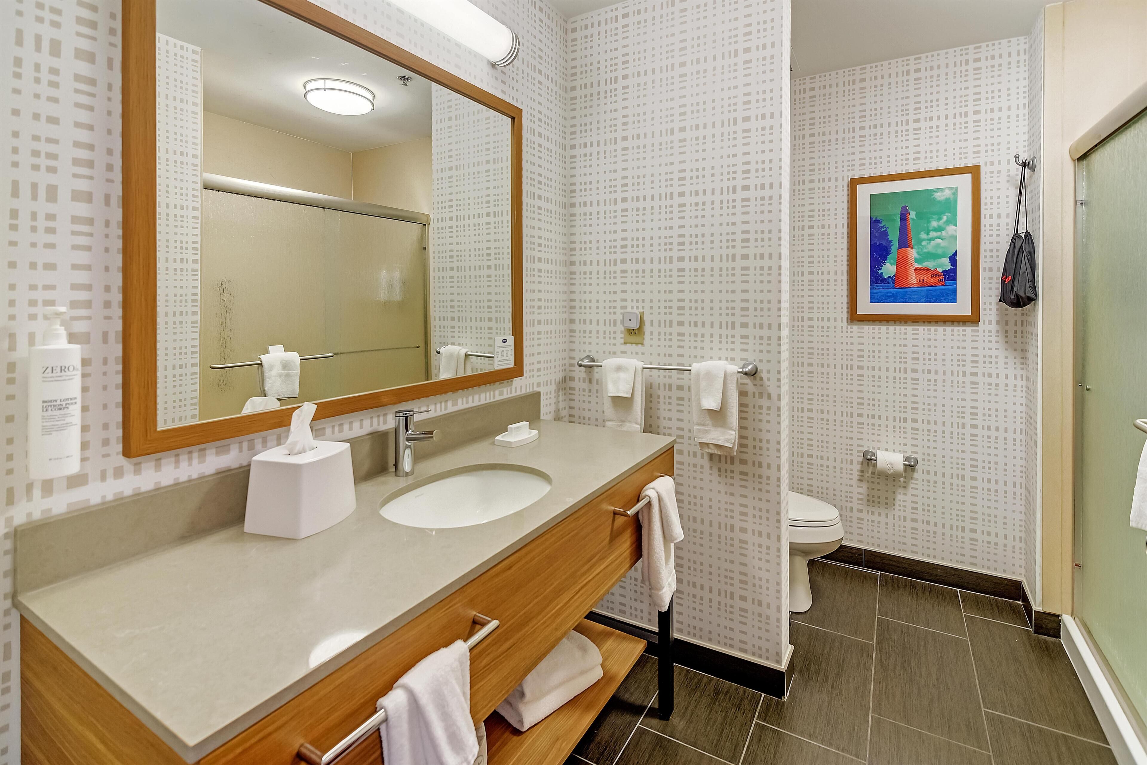 A bathroom with a wooden vanity, a large mirror, a sink, a toilet, and a framed picture on the wall.