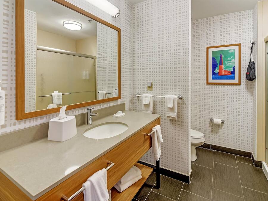 A bathroom with a wooden vanity, a large mirror, a sink, a toilet, and a framed picture on the wall.
