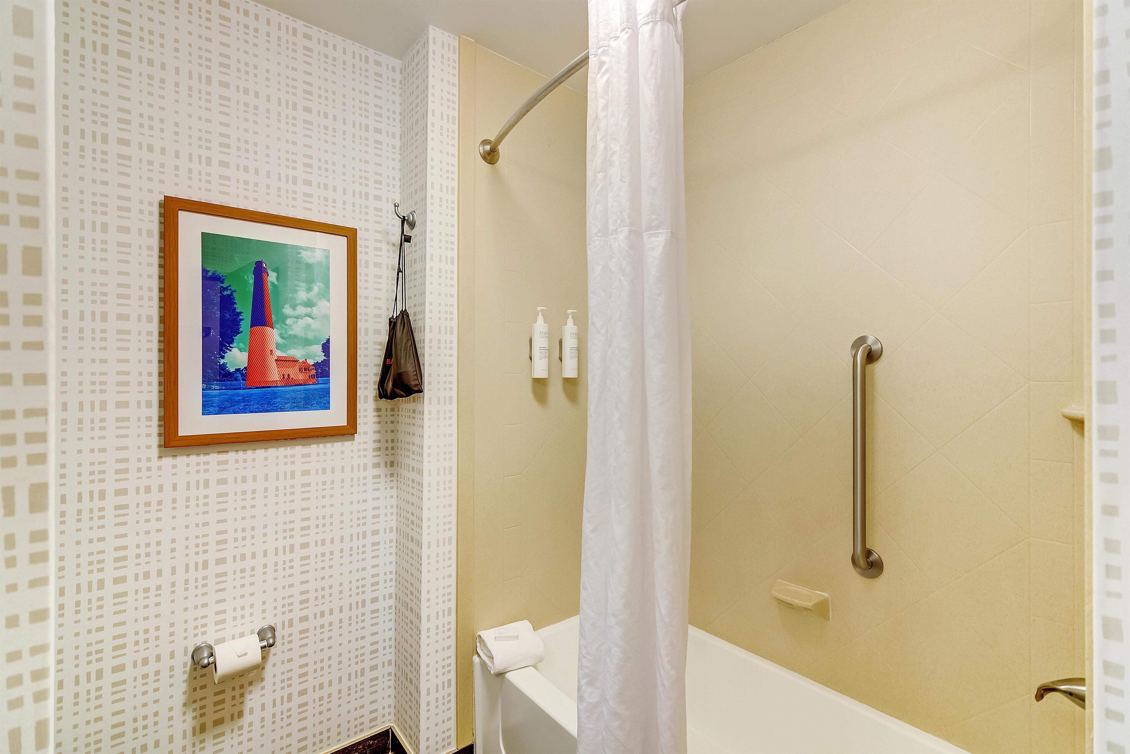 Une salle de bain équipée d’une douche, de toilettes, d’une baignoire, d’une barre d’appui, d’un porte-serviettes et d’un tableau encadré au mur.