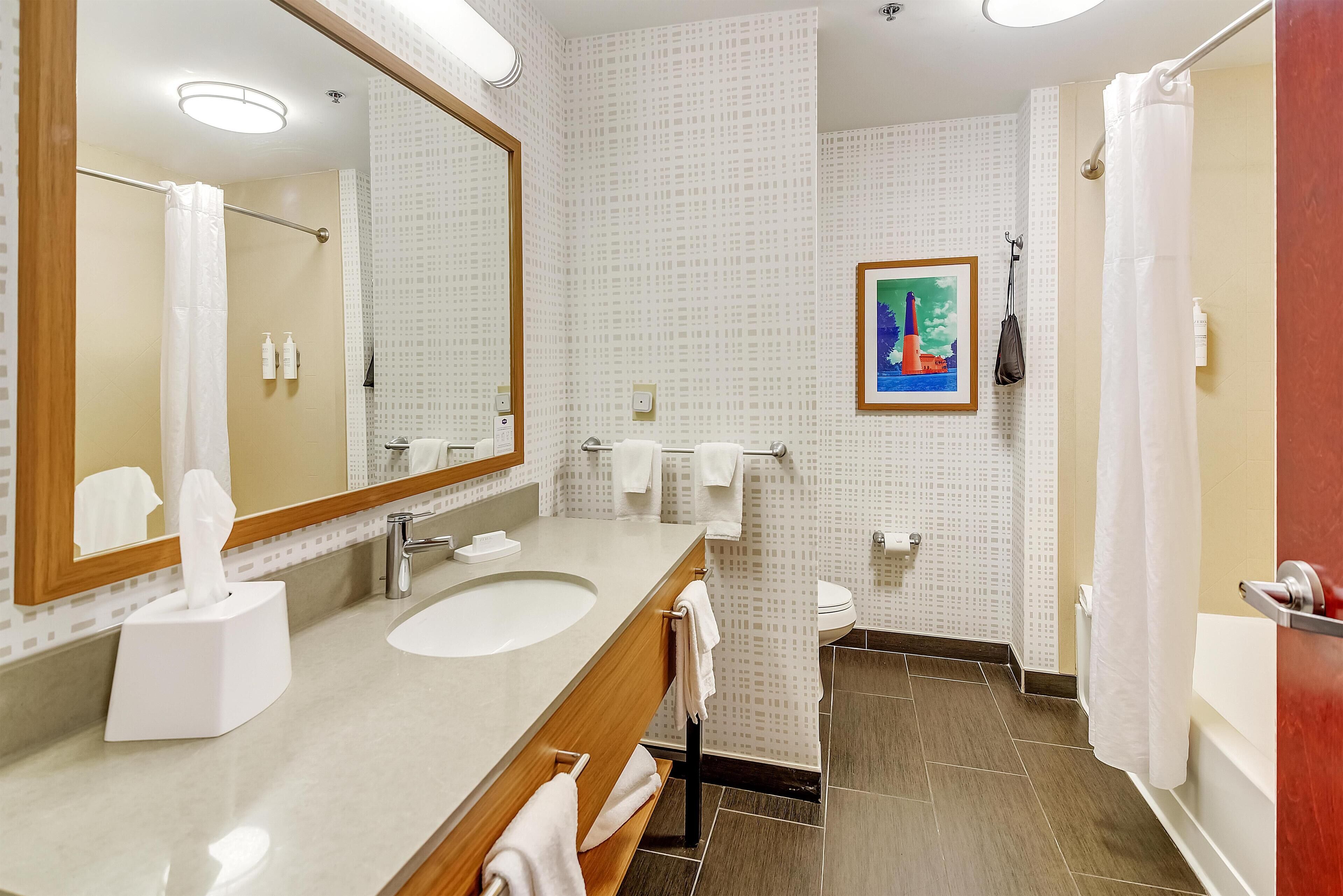 A bathroom with a large mirror, a sink, a toilet, and a shower.