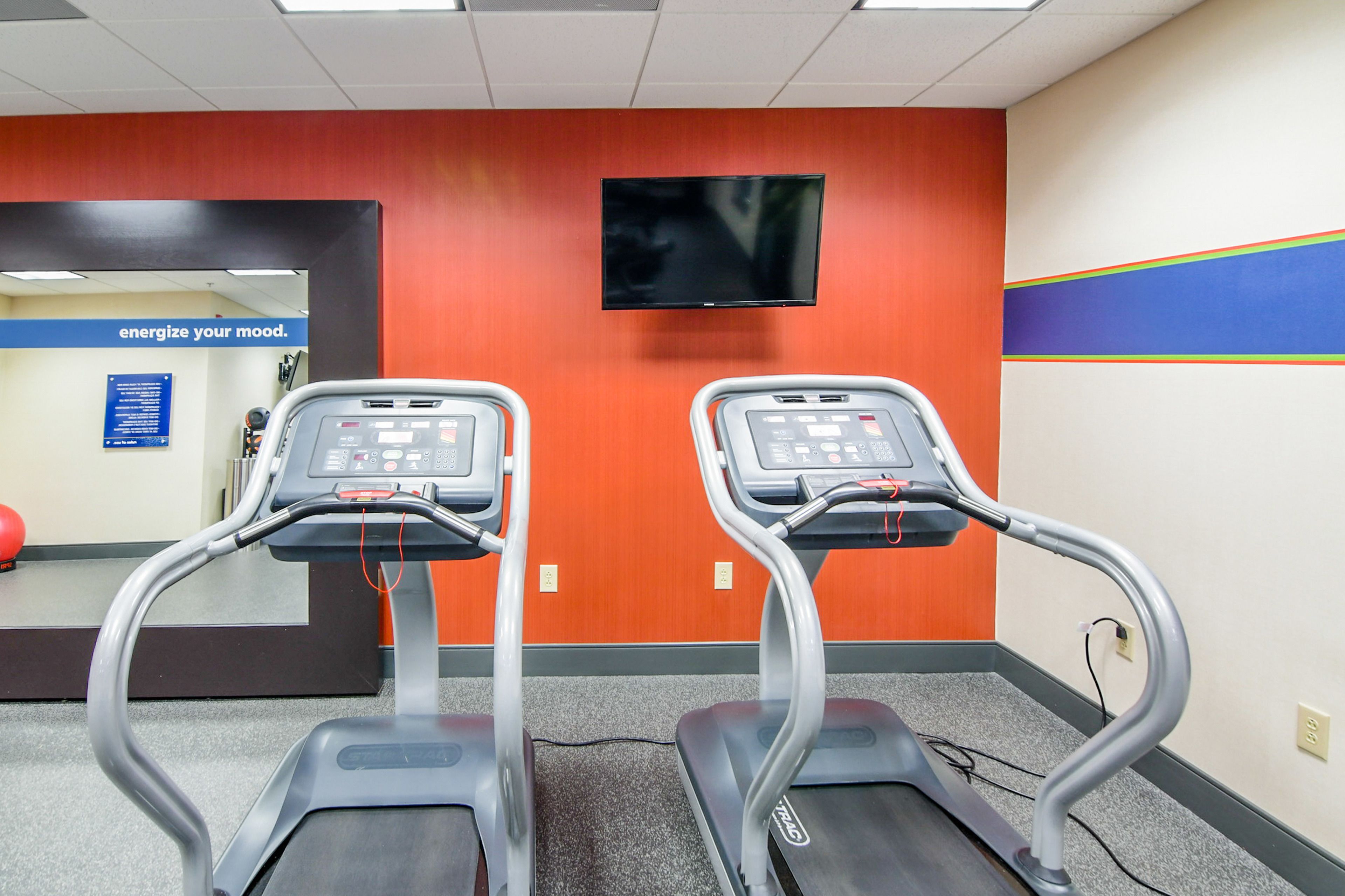 A gym with treadmills, a TV on the wall, and a motivational sign.
