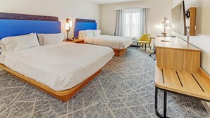Habitación de hotel con dos camas, un escritorio, una silla, una lámpara y un espejo grande.