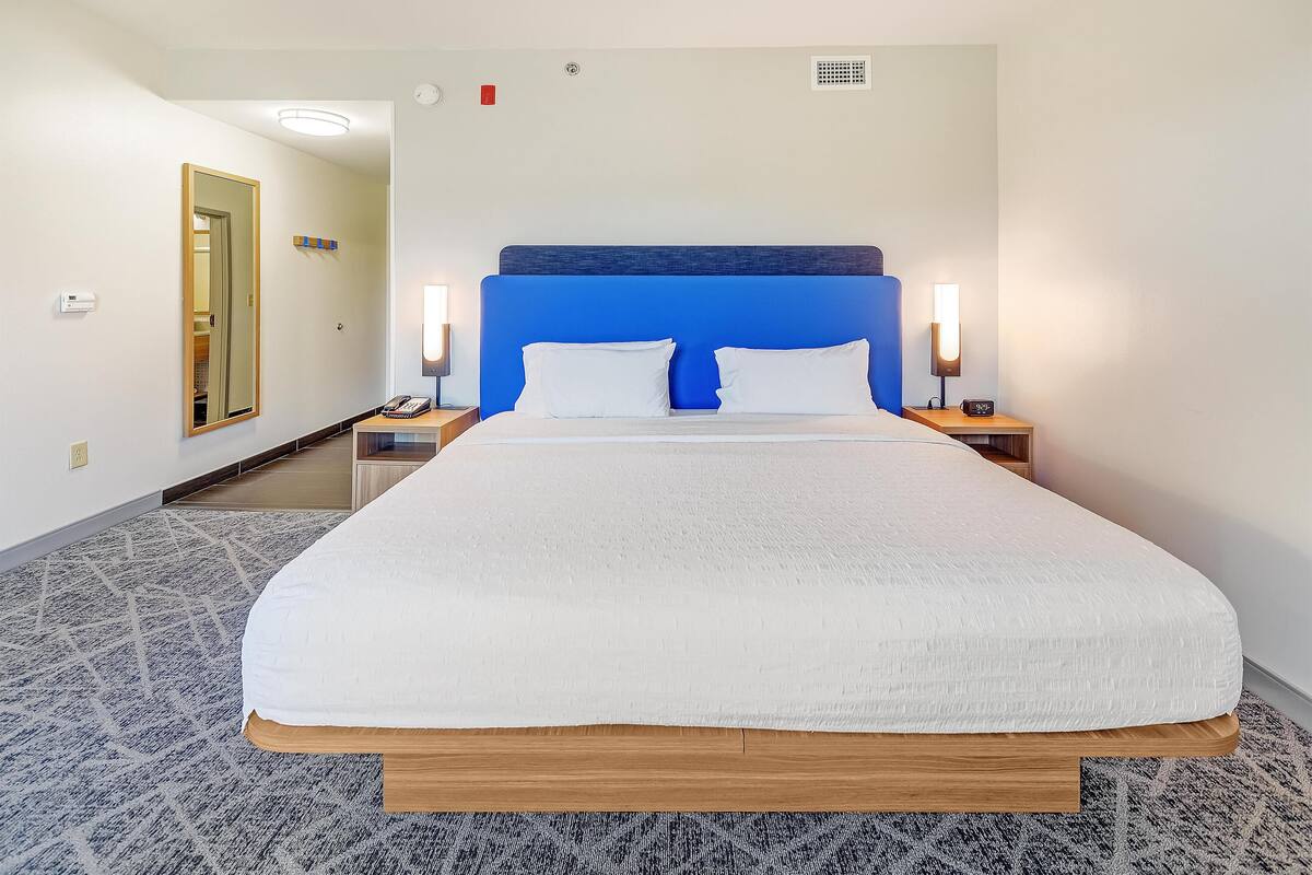 A hotel room with a large bed, two bedside lamps, and a mirror on the wall.