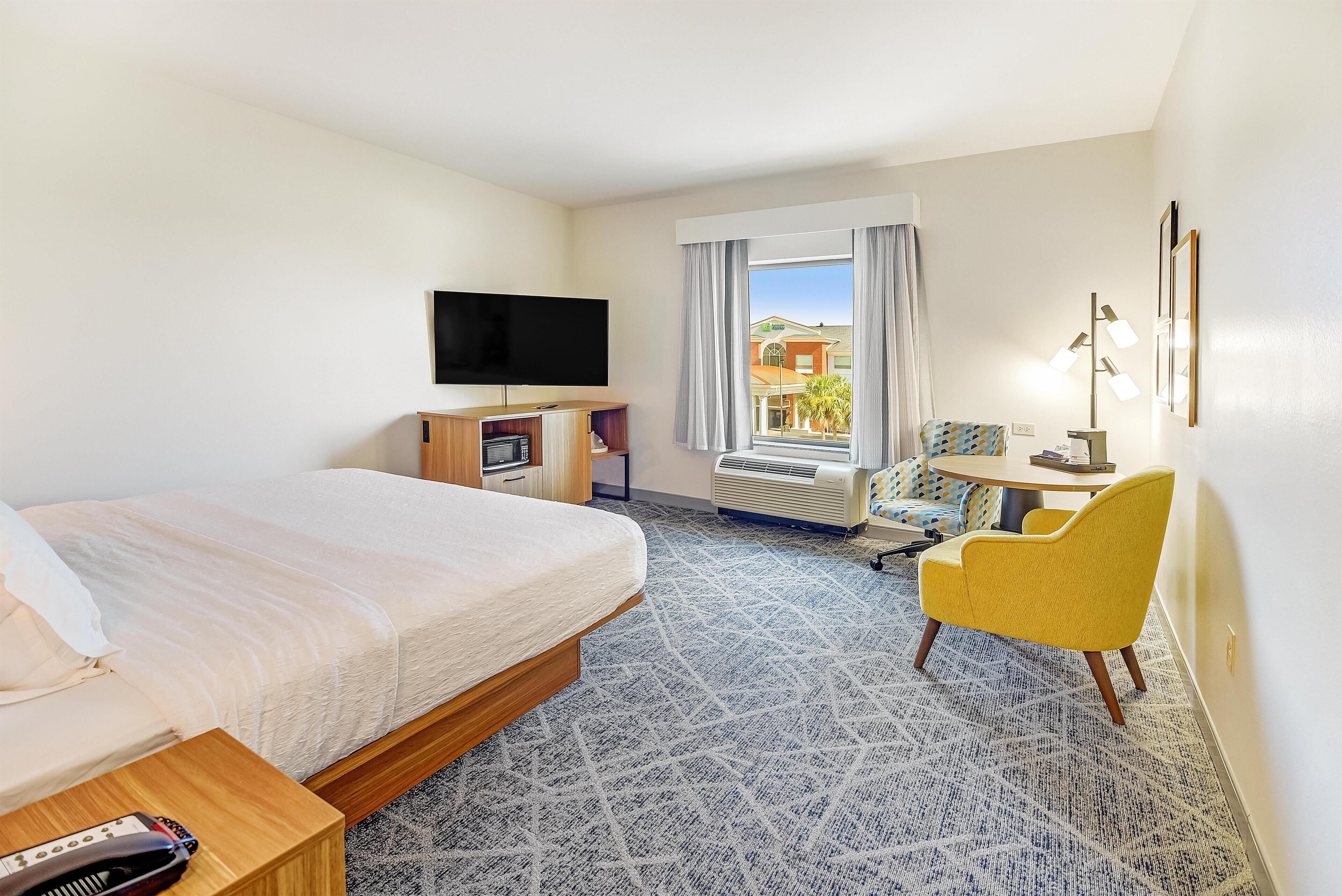 A hotel room with a bed, a TV, a desk, a chair, and a window with curtains.