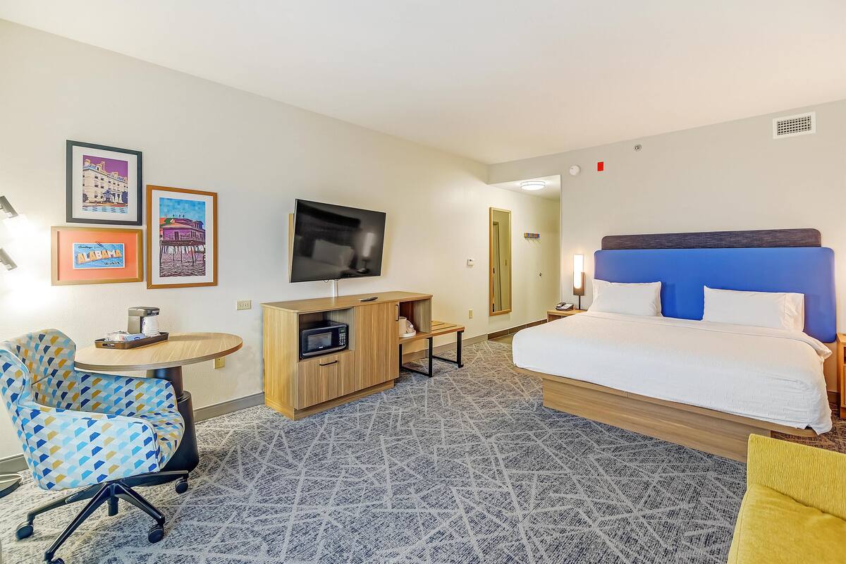 A hotel room with a bed, a desk with a TV, a chair, and a microwave.