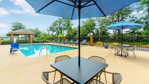 Un área junto a la piscina con mesa y sillas, un pabellón y sillones de descanso.