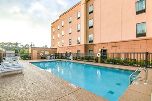 A swimming pool with lounge chairs and a building with multiple windows.