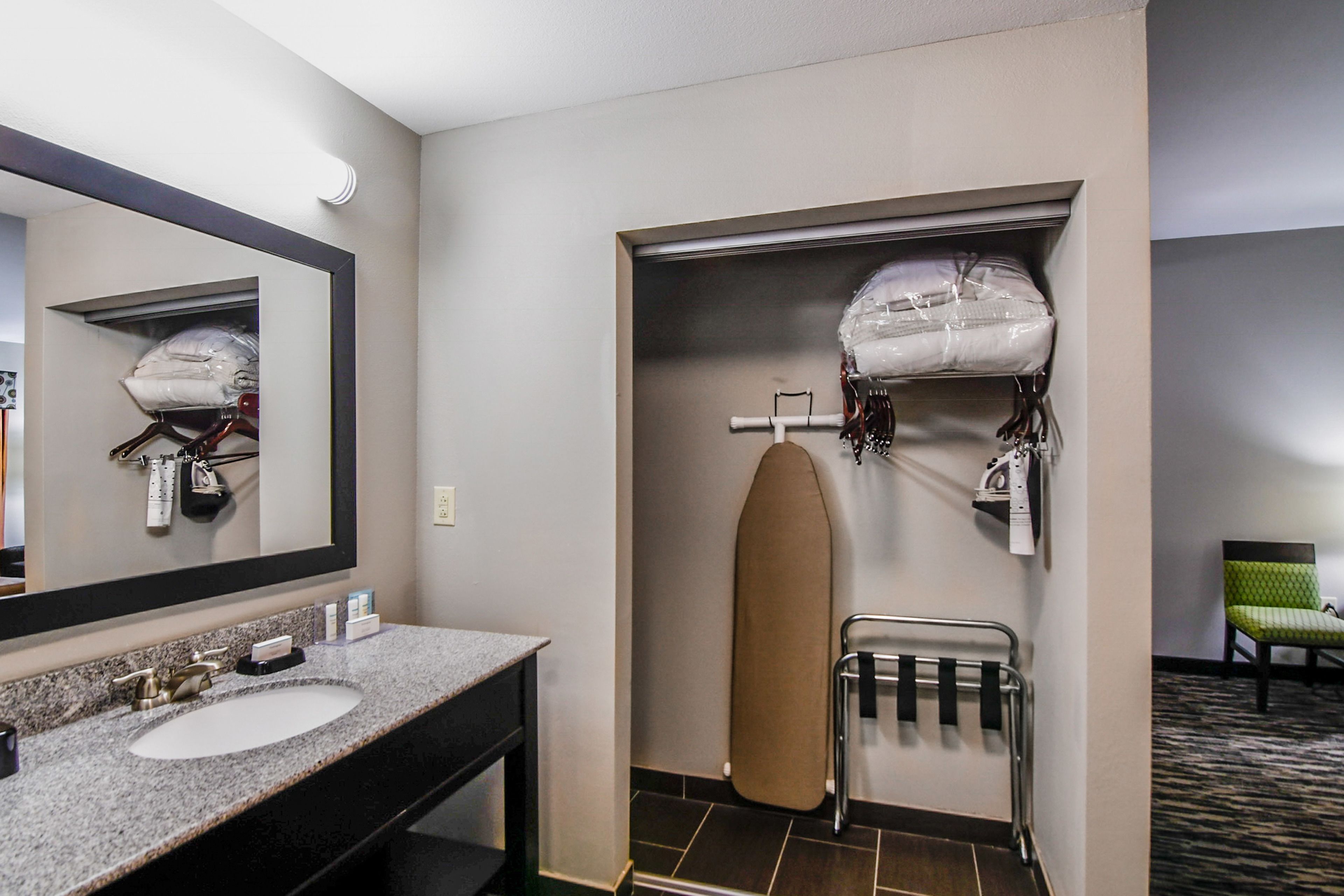 Une salle de bain d’hôtel équipée d’un lavabo, d’un miroir, d’un porte-serviettes et d’un espace de rangement contenant une grande serviette et un sac.