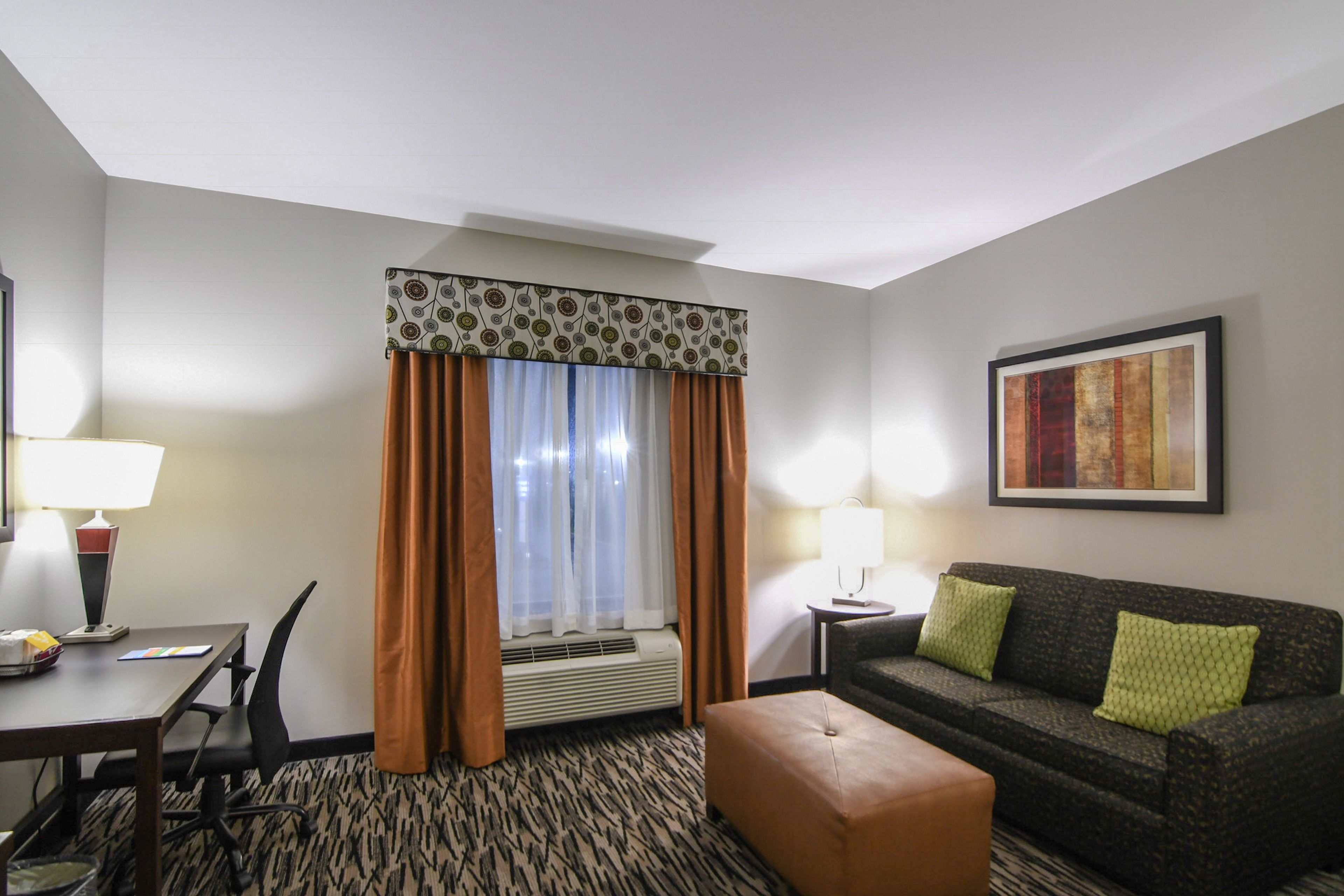 Une chambre d’hôtel comprenant une table à manger, un canapé, une fenêtre avec des rideaux, un tableau encadré au mur et une moquette à motifs.