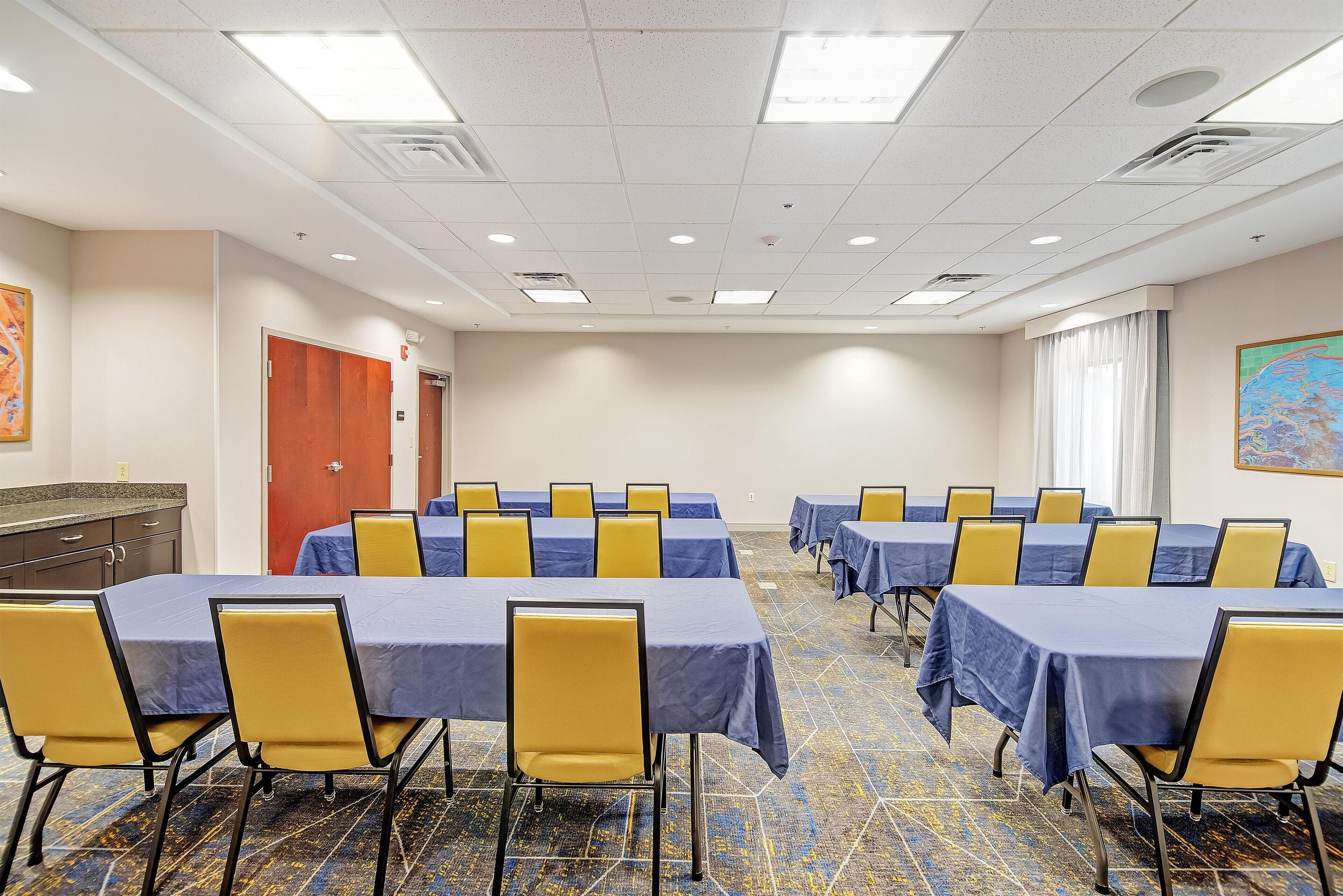 A conference room with tables and chairs, a door, and a window with curtains.