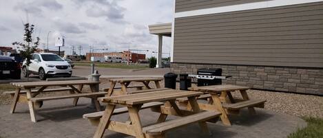 Un área de picnic al aire libre con mesas y bancos de madera, una parrilla y botes de basura.