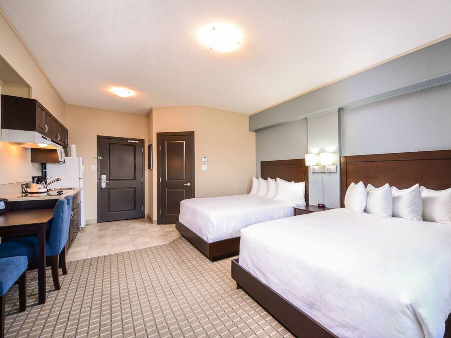 A hotel room with two beds, a desk, and a kitchenette.