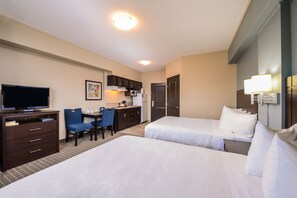 A hotel room with two beds, a desk with a chair, a television, a microwave, and a small kitchenette.