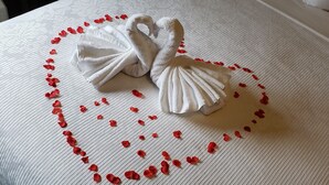 A neatly made bed with a heart-shaped arrangement of rose petals and two swan-shaped towels. - Chateau All Suites Hotel (Kindersley)