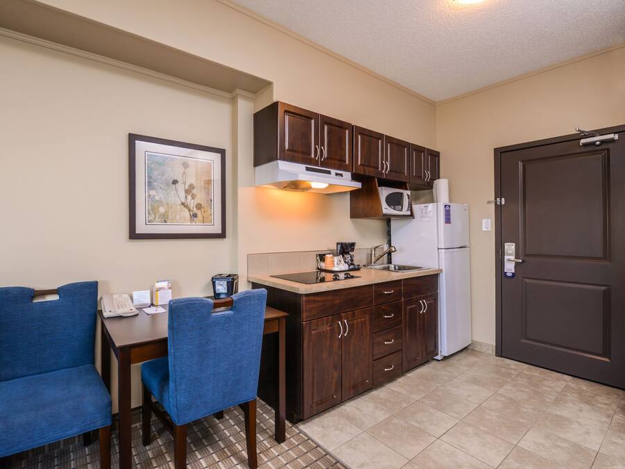 A compact kitchen with wooden cabinets, a microwave, a refrigerator, and a dining area with two blue chairs.