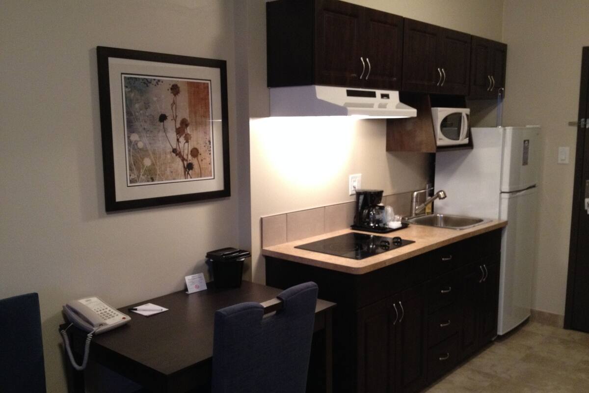 A compact kitchen with a microwave, stove, and sink. There's a framed artwork on the wall and a telephone on the table.