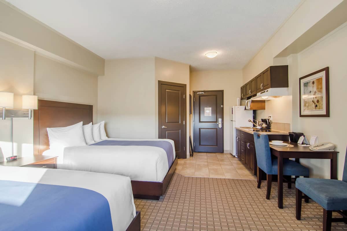 A hotel room with two beds, a kitchenette, a dining area, and a bathroom.