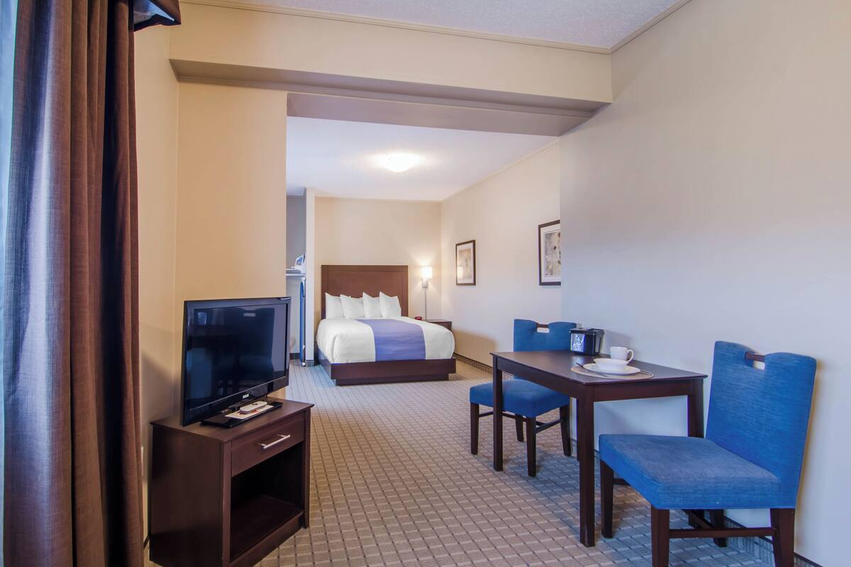 A hotel room with a bed, a TV, a desk with chairs, and a small table with a cup and saucer.