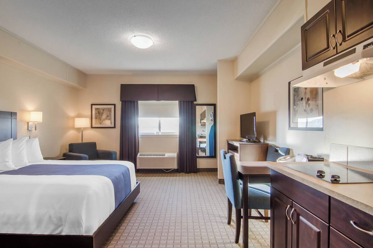 A hotel room with a bed, desk, chair, and kitchenette.