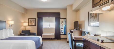 Una habitación de hotel con cama, escritorio, silla y kitchenette.