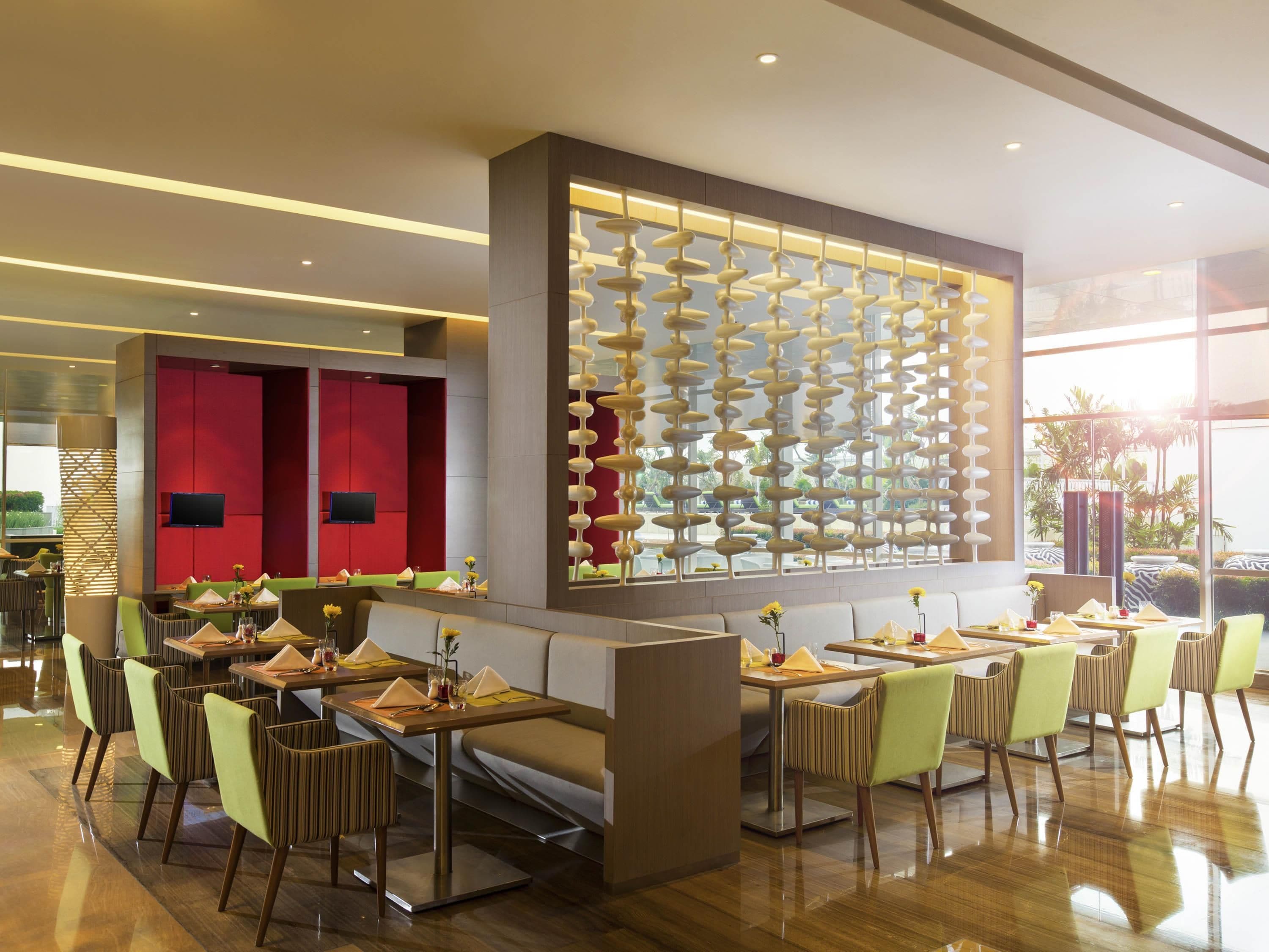 A modern restaurant with a central seating area, a red accent wall, and a decorative wall with hanging elements.