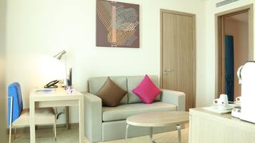 Una habitación de hotel moderna con sofá, una mesita, un escritorio con lámpara y una cafetera.