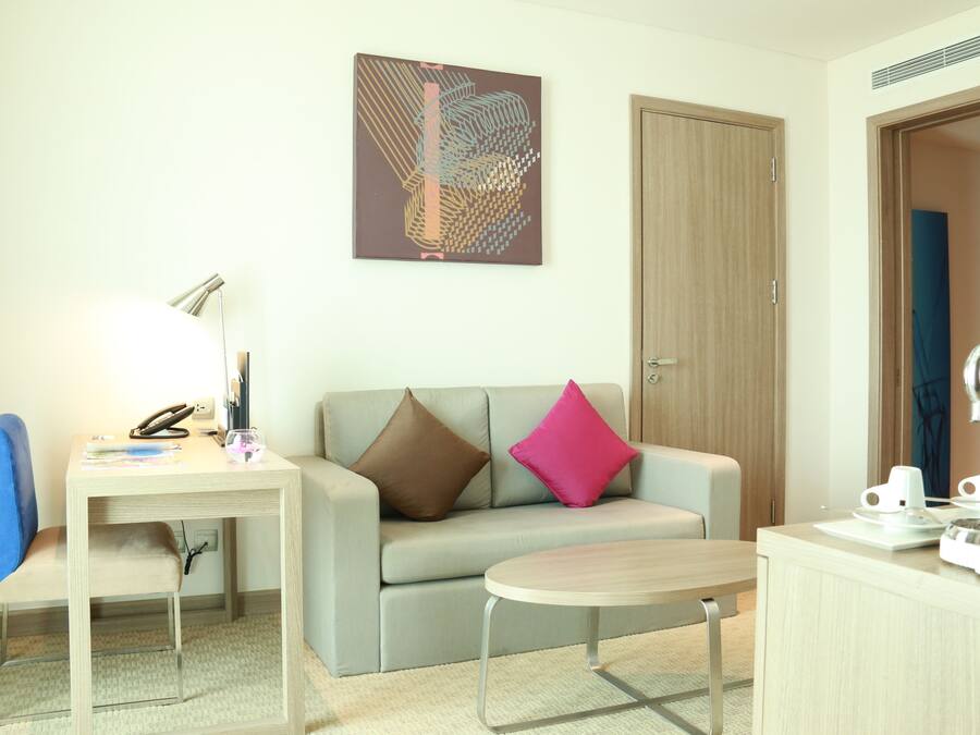 Una habitación de hotel moderna con sofá, una mesita, un escritorio con lámpara y una cafetera.