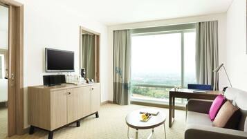 Habitación de hotel con televisor, una mesita con frutero, un sofá y un ventanal con vistas a la ciudad.