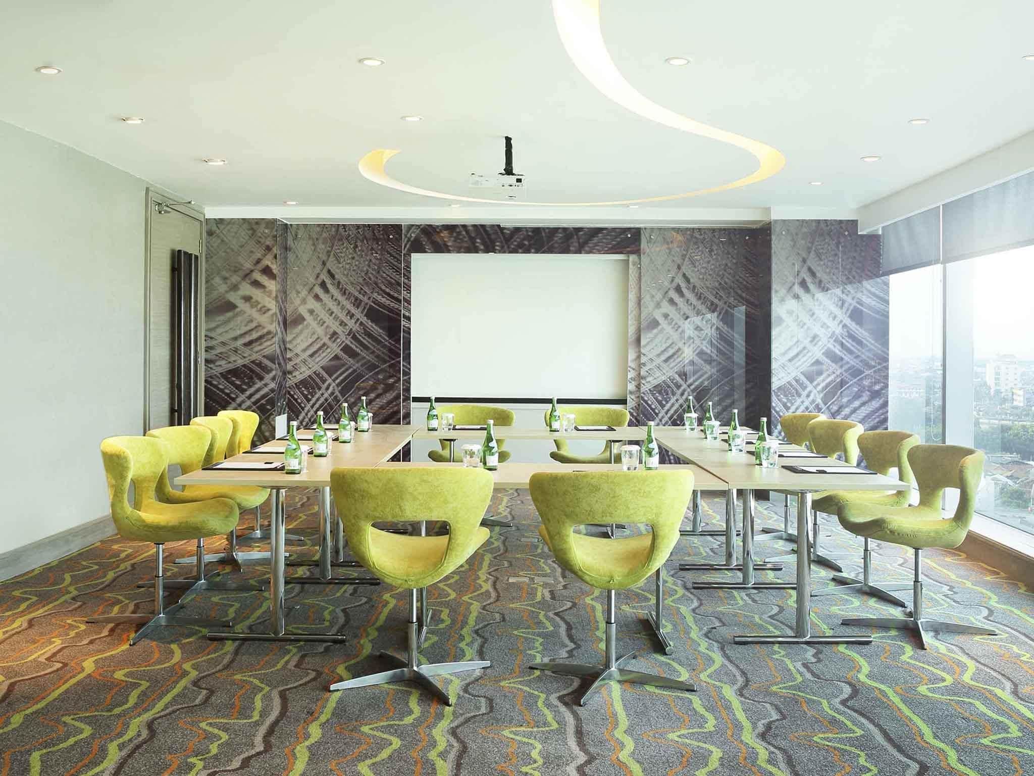 A conference room with green chairs, a large screen, and a patterned carpet.