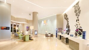 En moderne hotellobby med reception, siddeområde og en stor dekorativ væg.