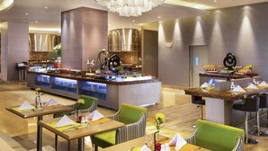 En moderne hotellobby med et centralt buffetbord, siddeområder og en stilfuld lysekrone.