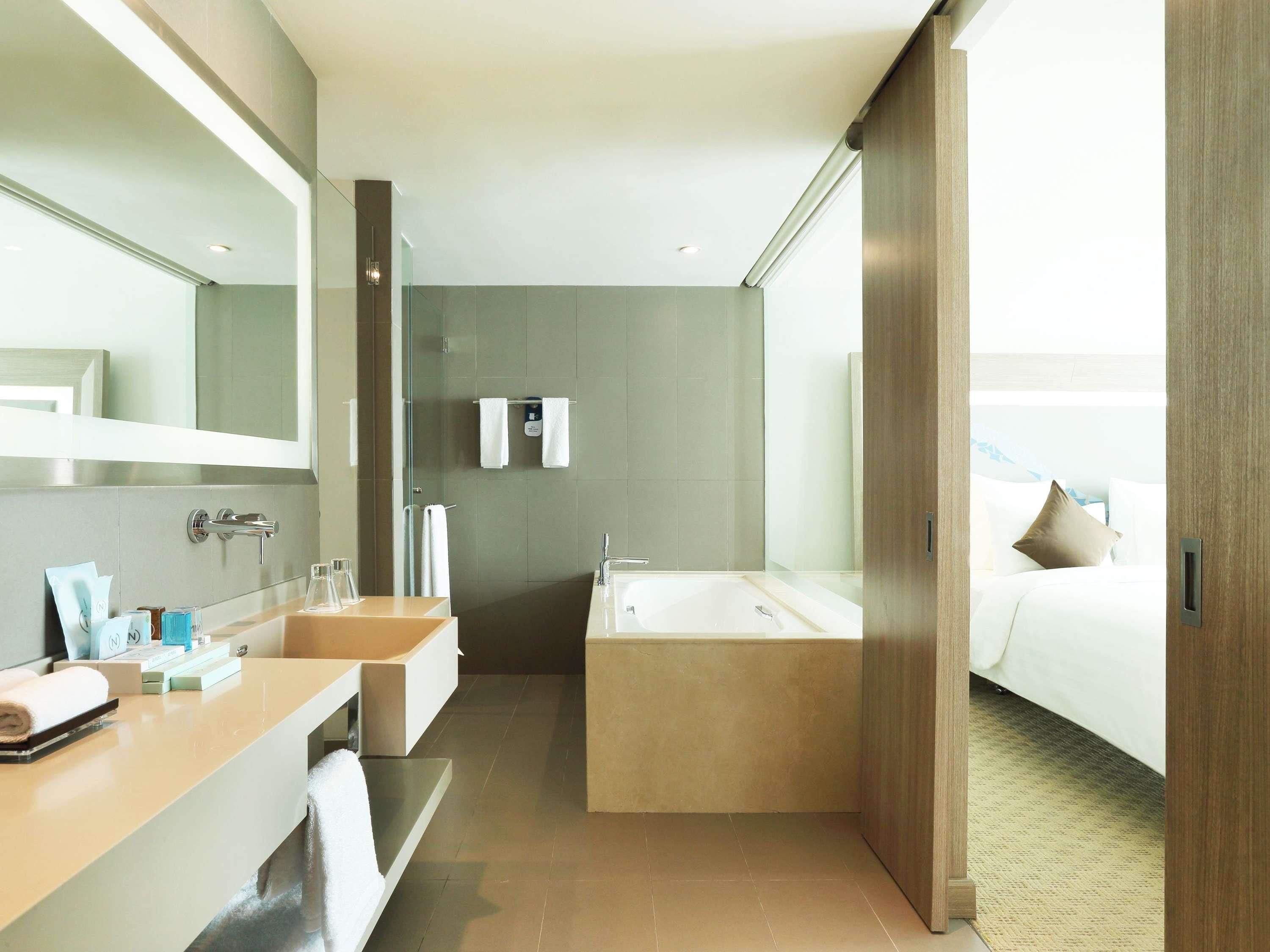 A modern hotel bathroom with a bathtub, two sinks, and a large mirror.