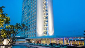 Et højt hotel med poolområde, kendetegnet ved et moderne design og en markant, lodret lysstribe på bygningen.