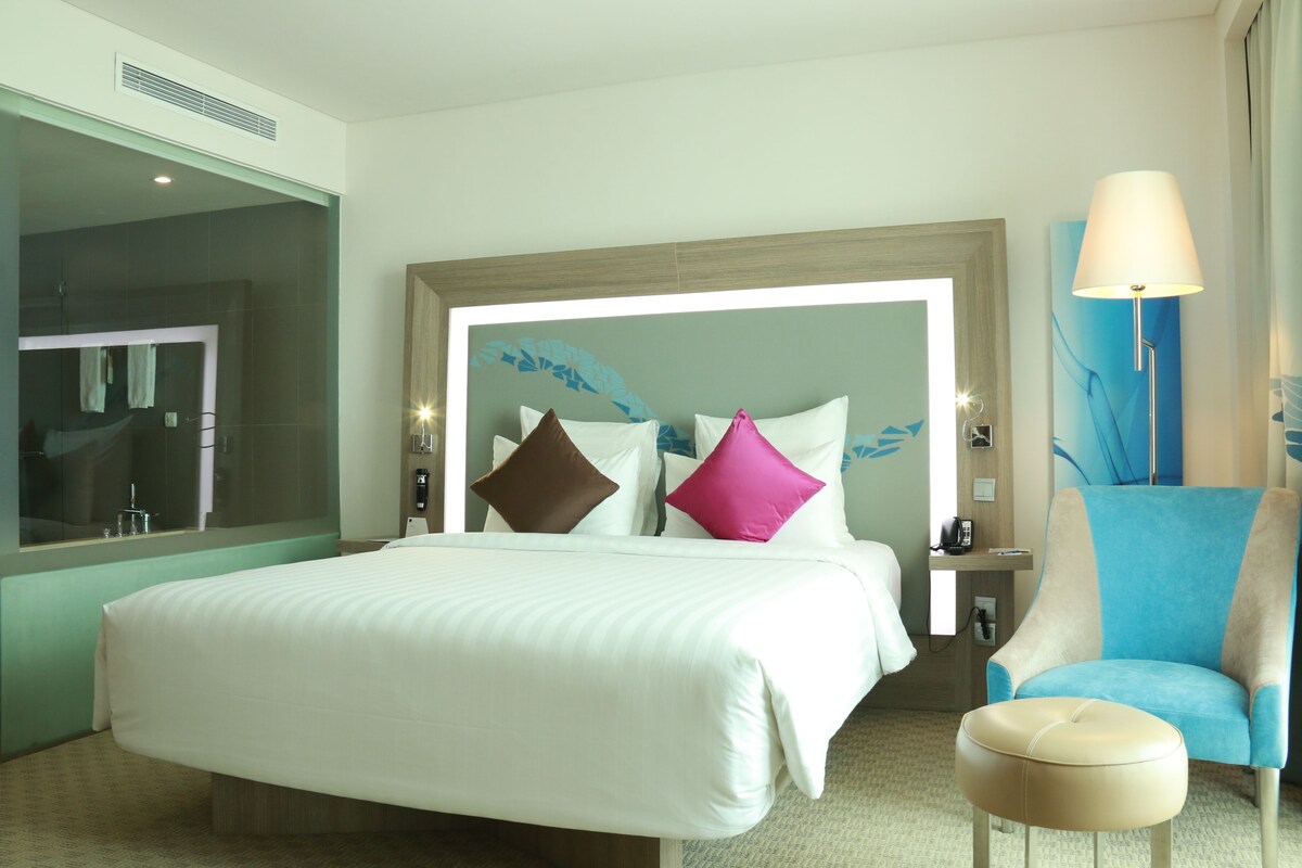 A hotel room with a large bed, a chair, and a small ottoman.