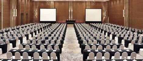 A conference room with rows of tables and chairs, large screens at the front, and a patterned carpet.