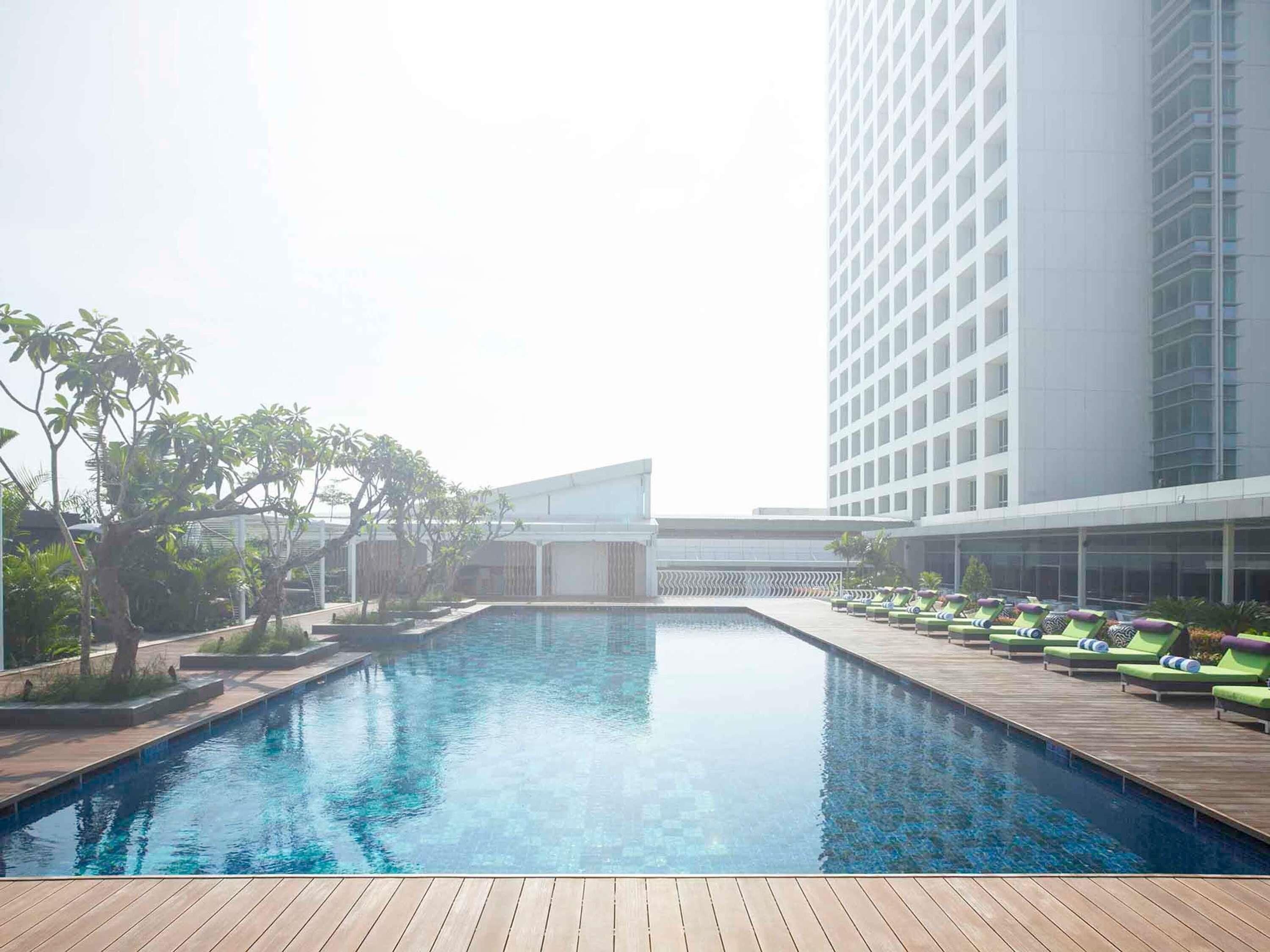 A swimming pool with lounge chairs, surrounded by greenery and modern buildings.