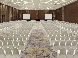 A conference room with rows of white chairs, a patterned carpet, and a modern ceiling design.