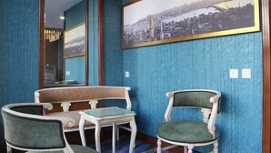 A room with a blue textured wall, a large framed cityscape picture, a wooden-framed mirror, a green upholstered sofa, a small white table, and two upholstered chairs. - Kaya Madrid Hotel (Istanbul)