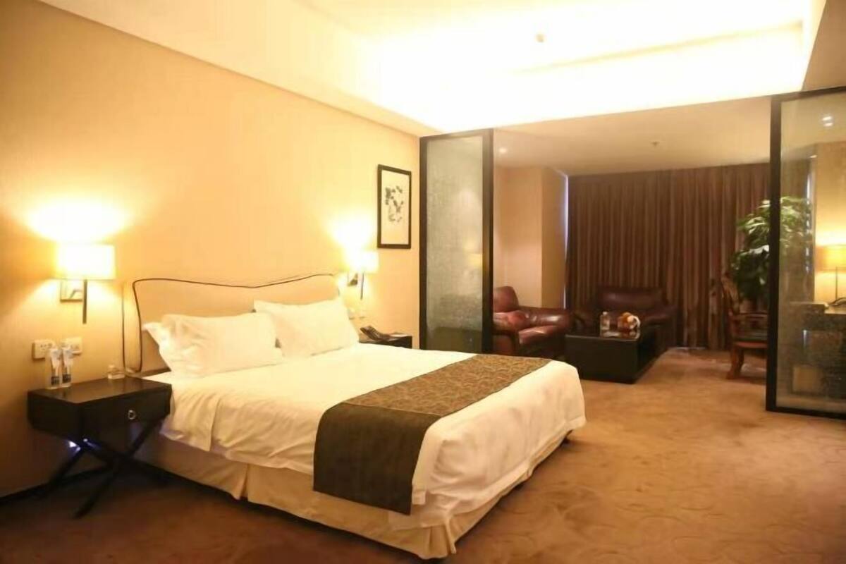 Ein Hotelzimmer mit einem großen Bett, Nachttischen, einem Schreibtisch, einem Sessel und einer Glaskonstruktion.