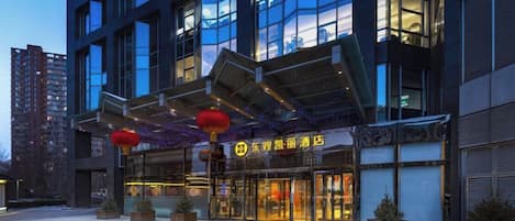A modern hotel with a glass facade, outdoor seating area, and a sign indicating a restaurant.
