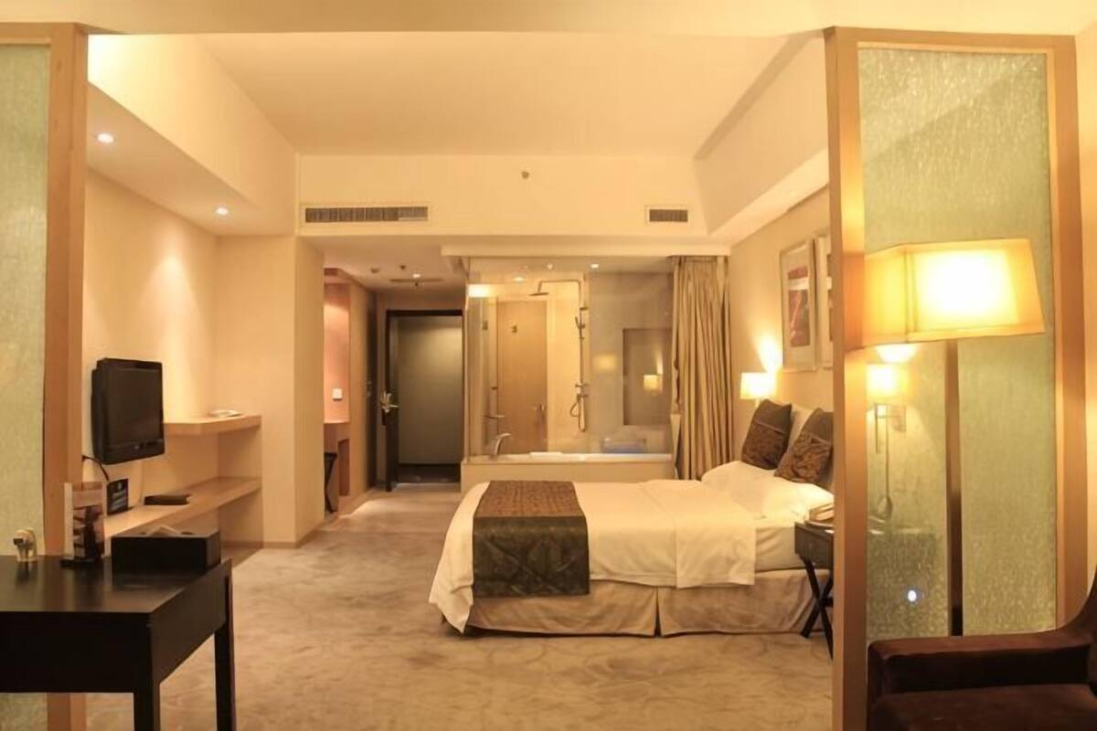 Ein Hotelzimmer mit Bett, Nachttisch, Fernseher und einem Badezimmer mit Dusche und Spiegel.