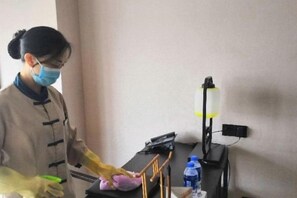 A person cleaning a table with a cloth and a spray bottle. - Donghuang Kaili Hotel (Beijing)