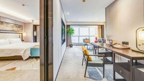 Una camera d'albergo moderna con un letto, una scrivania e un'area salotto, con una grande finestra e vista sulla città.