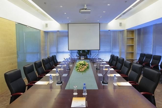 Una sala de conferencias con una mesa larga, varias sillas, una pantalla de proyector y un arreglo floral.