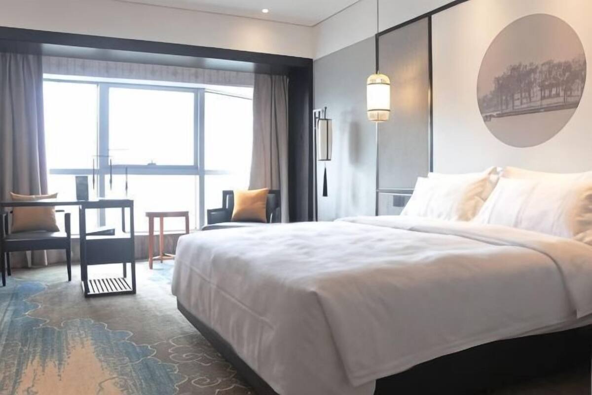 Ein Hotelzimmer mit einem großen Bett, einem Schreibtisch, einem Sessel und Blick ins Freie.