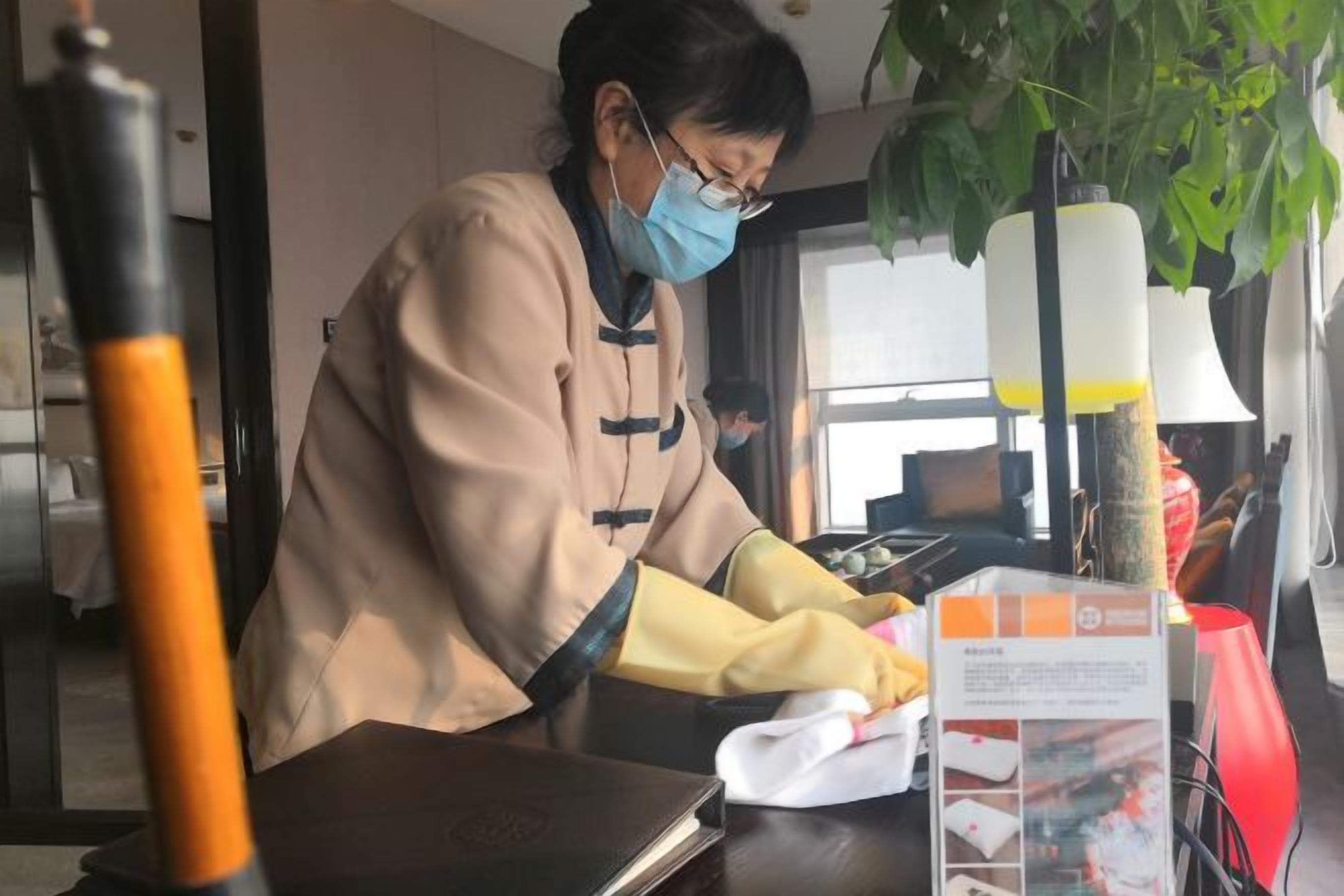A person working at a desk with a laptop, a plant, and a lamp in the background.