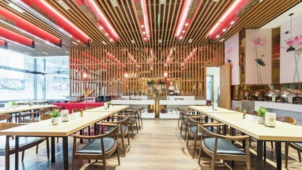Un interno ristorante moderno con tavoli e sedie in legno, una zona bar centrale e pannelli decorativi a parete.