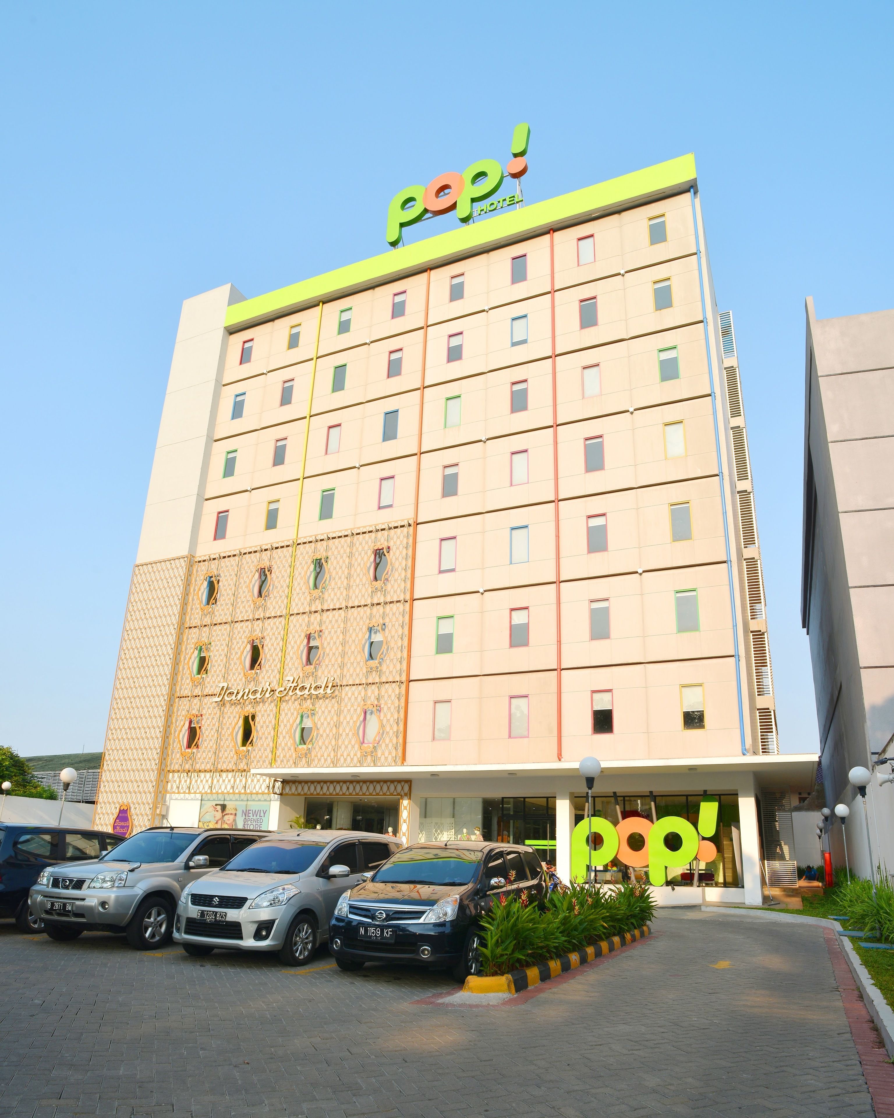 A hotel with a 'pop!' sign on the top, multiple floors, and a parking area with several cars.