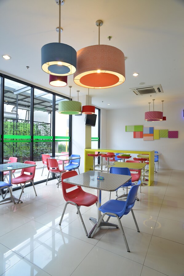 Un espace intérieur lumineux, agrémenté de chaises et de tables colorées, de grandes fenêtres et d’un design moderne au niveau du plafond.