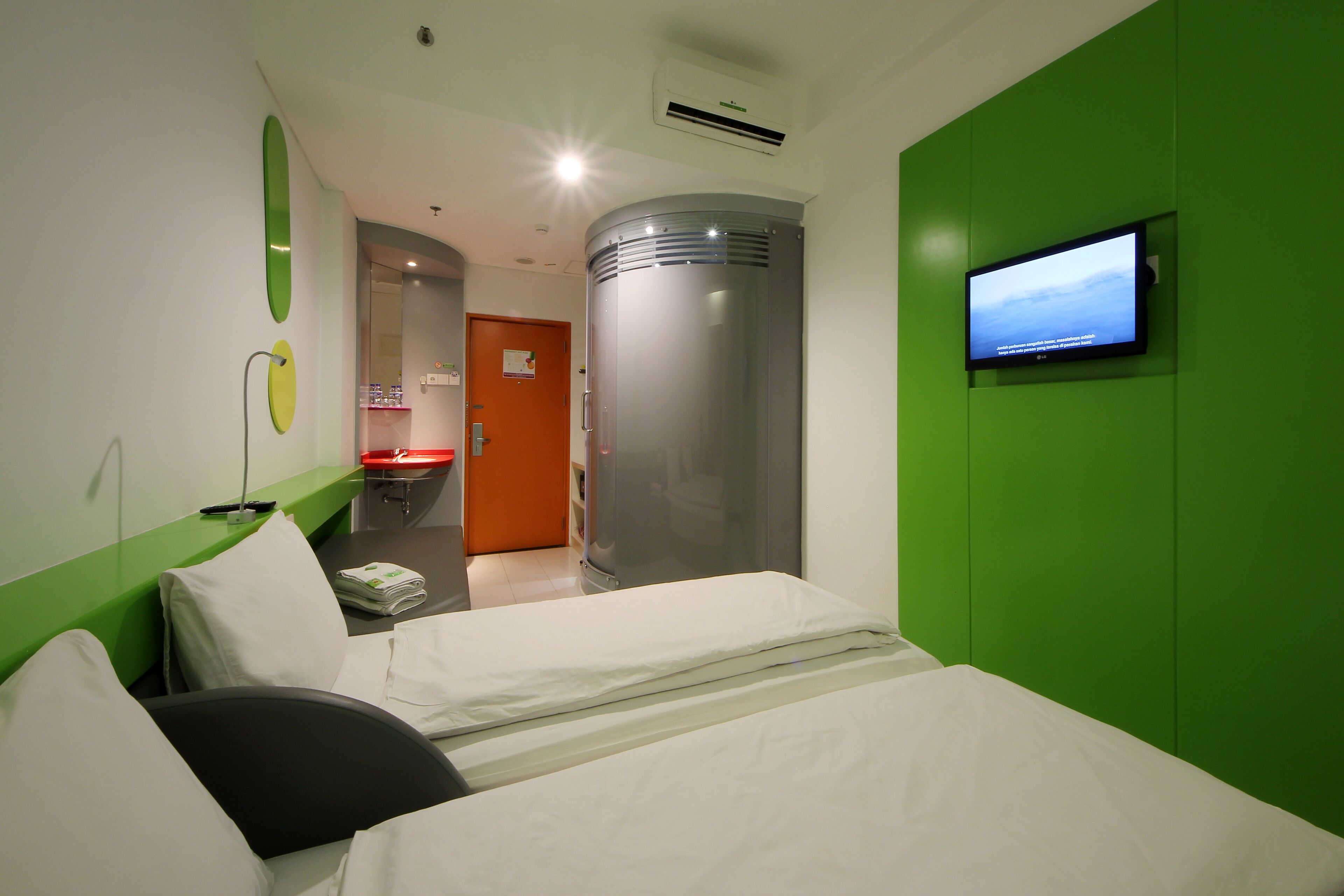 Une chambre d’hôtel comprenant un lit, un téléviseur fixé au mur, une salle de bain avec un lavabo et une porte donnant sur une autre pièce.